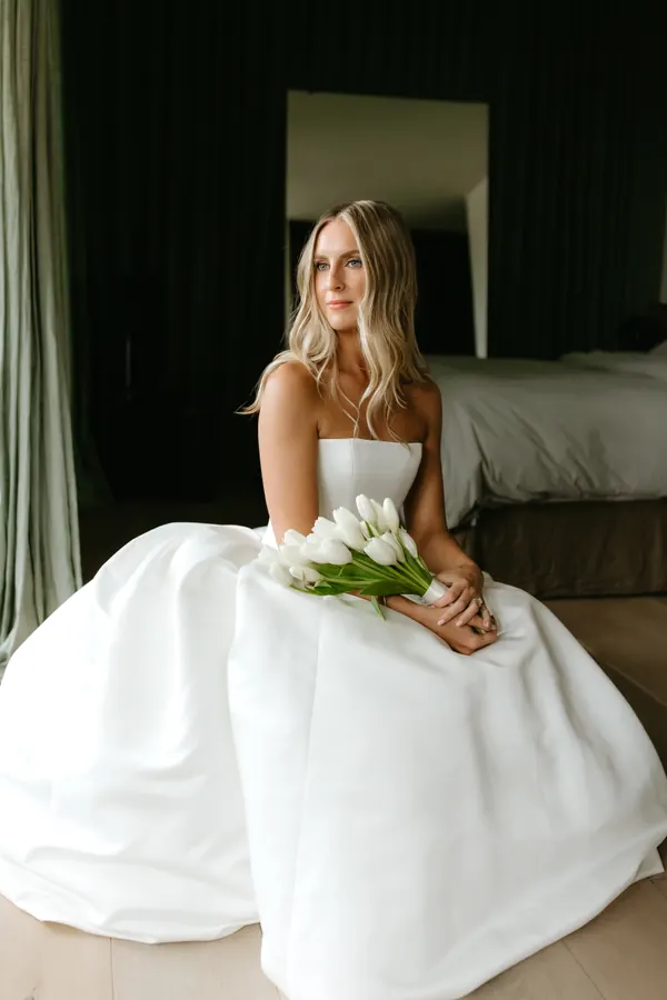 Seated on the bed in a full skirt holding white tulips, hair worn down